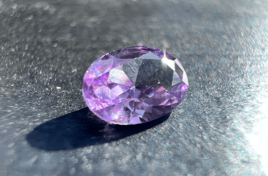 synthetic pink sapphire stone with color change on a neutral background and held by tweezers (gemmological tweezers) to illustrate the fancy sapphire.
