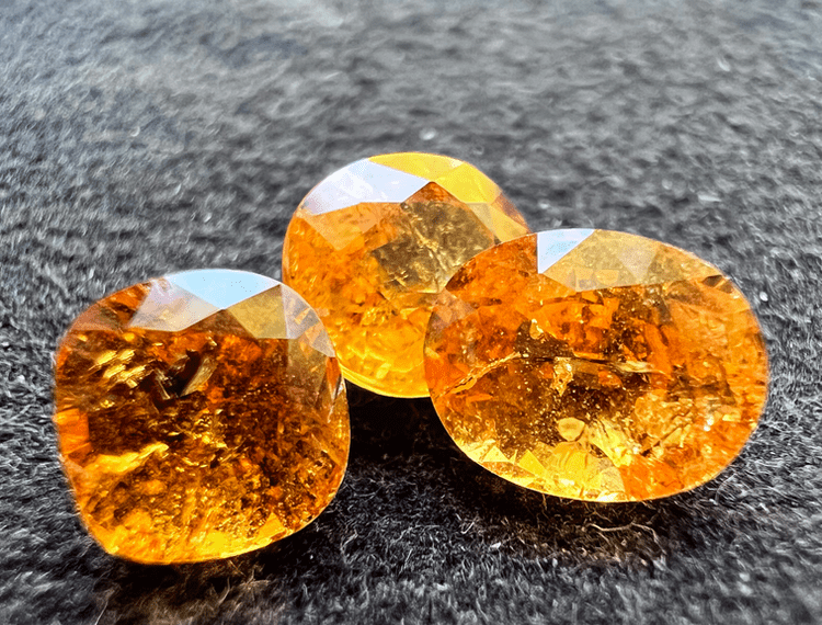 three orange spessartite garnet stones cut on a neutral background to illustrate spessartite and mandarin garnets